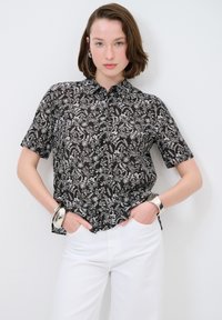 Camicia nera a maniche corte con un motivo floreale bianco, colletto a bottoni, dal taglio rilassato abbinata a pantaloni bianchi a gamba larga.