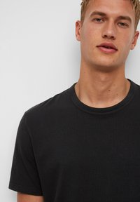 Czarny bawełniany t-shirt z okrągłym dekoltem i krótkimi rękawami, charakteryzujący się gładką teksturą i minimalistycznym designem.