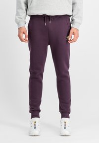 Lila Jogginghose aus weichem Material mit elastischem Bund, verstellbarem Kordelzug, gerippten Säumen und kleinem Logo an der Seite.
