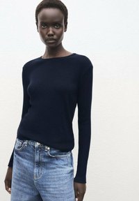 Dunkelblauer langärmliger Strickpullover mit Rundhalsausschnitt, kombiniert mit hellblauen hochgeschnittenen Jeans. Der Stoff wirkt glatt und enganliegend.