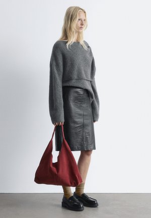 Grauer Strickpullover, schwarze Bleistiftrock mit Krokodilprägung, roter Wildleder-Schultertasche und schwarze Loafers mit gelben Rippensocken.