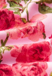 Blommig tyg med en rosa bakgrund, med stora röda rosor och gröna blad. Texturen är slät och något glansig.