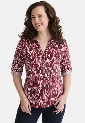 Rotes gemustertes Hemd mit kurzen Ärmeln, das eine Knopfleiste auf der Vorderseite und abstrakte weiße Designs aufweist, aus leichtem Stoff gefertigt.