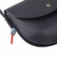 Borsa in pelle blu navy con pattina curva, cuciture tono su tono e una tracolla annodata. Presenta un piccolo accento rosso alla chiusura per un tocco di dettaglio.