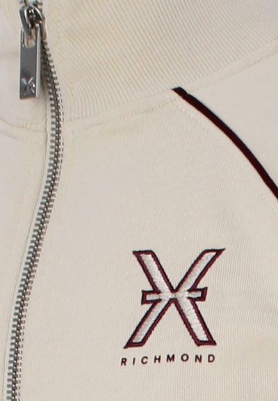 Giacca zip-up crema realizzata in tessuto morbido. Presenta dettagli bordeaux, un logo "X" in evidenza e colletto e polsini a coste. Zip frontale.