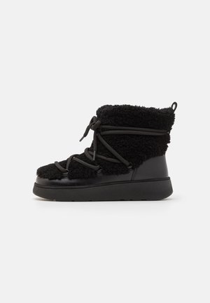 Black ankle boots featuring a combination of plush, fuzzy texture and sleek leather. Thick sole with adjustable laces and a pull tab at the back.