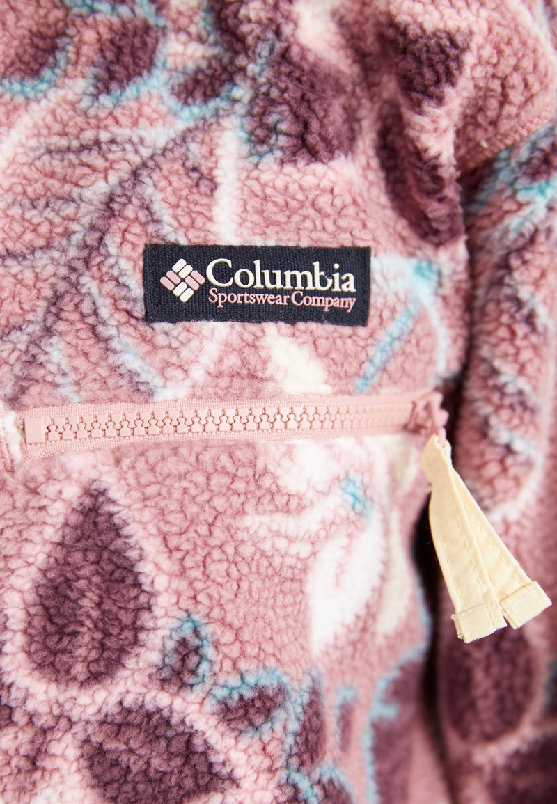 Pull en polaire dans des tons pastel de rose et de violet avec des accents bleus, comportant une poche zippée et un patch logo Columbia sur la poitrine.