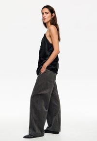 Camisón de satén negro con ribete de encaje, combinado con pantalones de pierna ancha grises de textura suelta. Zapatos negros de punta afilada completan el conjunto.