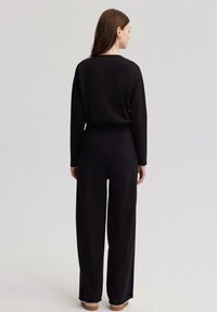 Conjunto de ropa negra que incluye una camiseta de manga larga y pantalones de pierna ancha, fabricado en una tela suave con cinturilla elástica, textura suave y diseño minimalista.