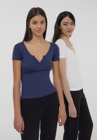 Due magliette attillate, una blu navy con maniche corte e scollatura a bottoni, e una bianca con maniche corte e scollatura a V, abbinate a pantaloni neri.