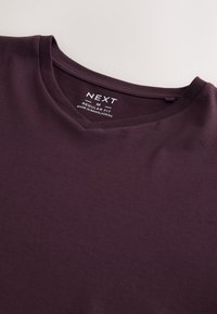 Camiseta de algodón de color púrpura oscuro con cuello en V y etiqueta "NEXT M Regular Fit Made in Bangladesh" dentro del cuello.