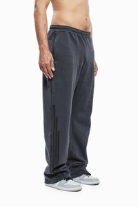 Grå træningsbukser med elastisk talje, sidelommer og tre mørke striber langs ydersiden af benene. Et par lysegrå sneakers er synlige.