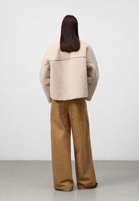 Beżowa kurtka z owczej wełny o pudełkowym kroju, szerokimi rękawami i detalem szwu z tyłu, połączona z khaki spodniami o szerokich nogawkach z tylnymi kieszeniami.