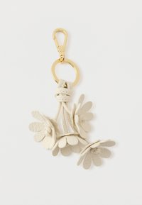 Skórzany brelok do kluczy z trzema kwiatami w kształcie płatków w kolorze lekko białym, połączonymi teksturowanym sznurkiem oraz złotym klipsem i pierścieniem.