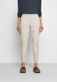 Chinos beige clair à coupe fuselée, en coton. Associés à un haut à manches longues foncé et des sandales noires à enfiler à semelle plate.