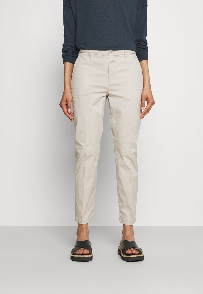 Chinos beige clair à coupe fuselée, en coton. Associés à un haut à manches longues foncé et des sandales noires à enfiler à semelle plate.