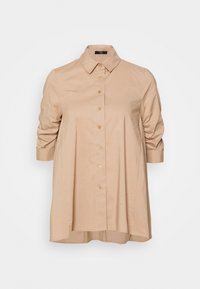 Camicia beige chiaro con colletto classico, chiusura frontale con bottoni e maniche corte a sbuffo. Tessuto morbido con una vestibilità leggermente rilassata.