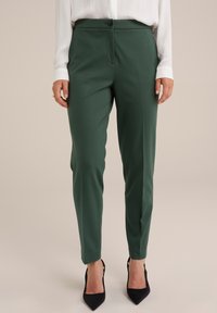 Groene tailored broek gemaakt van een gestructureerde stof. Heeft een slim fit, voorzakken en een sluiting met één knoop. Geschikt voor zwartgekleurde hakken.