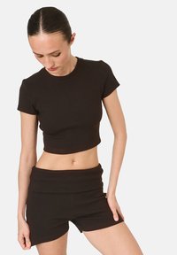 Čierny rebrovaný bavlnený crop top s krátkymi rukávmi a okrúhlym výstrihom, kombinovaný s vysokými šortkami v rovnakom štýle. Diskrétne logo na vrchu.
