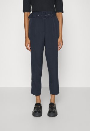 Marineblauwe high-waisted broeken met een riem en gesp-detail, met geplooide voorzijde en een taps toelopend ontwerp, gecombineerd met zwarte instappers.