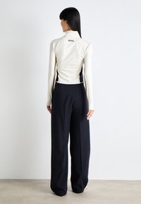 Top aderente a maniche lunghe color crema con pannelli laterali neri e colletto, abbinato a pantaloni larghi blu scuro. Tessuto testurizzato e logo del marchio sul retro.