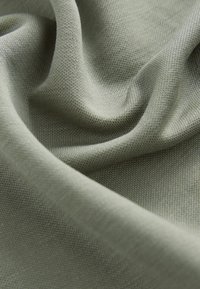 Tissu vert clair avec une texture douce et un motif fin tissé, drapé en plis délicats, présentant un matériau lisse et flexible.