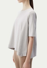 Ljusgrå bomullstop med kort ärm, avslappnad passform, rundad halsringning och något kortad nederkant, i kombination med ribbade bruna leggings.