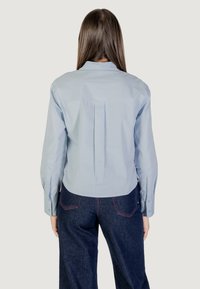 Camicia azzurra chiara a maniche lunghe con colletto e dettaglio a pieghe sulla schiena, abbinata a jeans in denim scuro a vita alta con accenti di cucitura a contrasto.