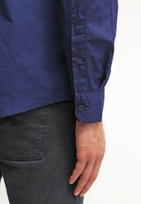 Mörkblå långärmad skjorta i bomull med manschettknäppning, med en jämn yta och en lätt glans. Kombinerad med mörkgrå denim.