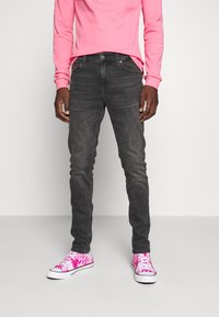Skinny dark gray jeans paired with vibrant pink and white tie-dye sneakers, worn with a long-sleeve pink shirt.