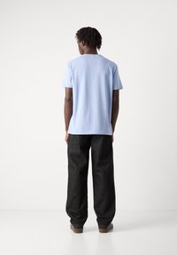 Šviesiai mėlyna medvilninė t-shirt su trumpomis rankovėmis ir apvaliu iškirpimu, derinama su juodais plačiais džinsais ir rudais batais, matoma iš nugaros.