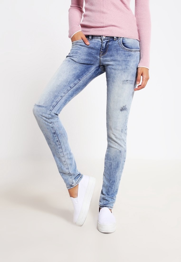 Vaaleansiniset skinny-farkut, joissa on kulutuksia, viisi taskua ja haalistunut pesu. Yhdistetty valkoisiin liukuvaihdettaviin tennareihin ja vaaleanpunaiseen ribbiknitti-svetariin.