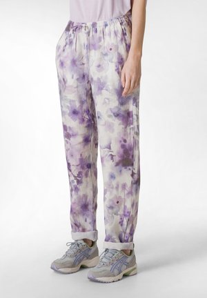 Pantaloni leggeri con motivo floreale in lavanda e crema, dotati di una cintura elastica, vestibilità ampia e orli arrotolati. Abbinati a sneakers grigie.