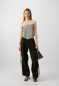 Haut sans manches à rayures noires et blanches, pantalons cargo oversize vert foncé avec poches et cordons, et un petit sac à main argenté clouté.