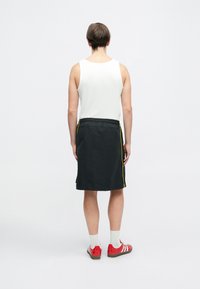 Svart idretts skjørt med gule sidestriper, elastisk midje, brukt over en hvit tank topp. Kombinert med røde joggesko og hvite sokker.