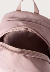 Ανοιχτό ροζ σακίδιο με κλείσιμο με φερμουάρ, διαθέτει υφασμάτινη υφή και απαλό επένδυση στο εσωτερικό με διακριτικό σχέδιο λογότυπου.