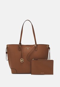 Bruine lederen totebag met dubbele handvatten, voorzien van een gouden MK-hanger en een bijpassend ritszakje. Soepele textuur, minimalistisch ontwerp.