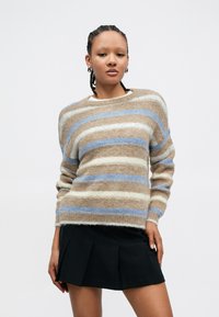 Stripete genser i tan, krem og lyseblå; myk tekstur med en avslappet passform; rund hals, båret over et svart plisset skjørt.