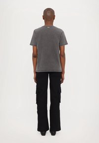 Camiseta de algodón gris con mangas cortas, detalle en la costura trasera, combinada con pantalones cargo negros con bolsillos laterales y un dobladillo acampanado.