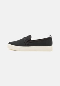 Svarta canvas slip-on skor med en flätad detalj på ovandelen, med en vit gummisula, minimalistisk design och utan synliga stängningar.
