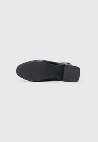 Sapato de couro preto com salto quadrado, superfície lisa e sola de borracha texturizada. Apresenta um design de corte baixo e detalhes mínimos em metal.