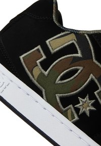 Čierne semišové tenisky s vyšívaným maskáčovým logom, bielou gumovou podrážkou a kontrastným prešívaním pozdĺž okrajov.