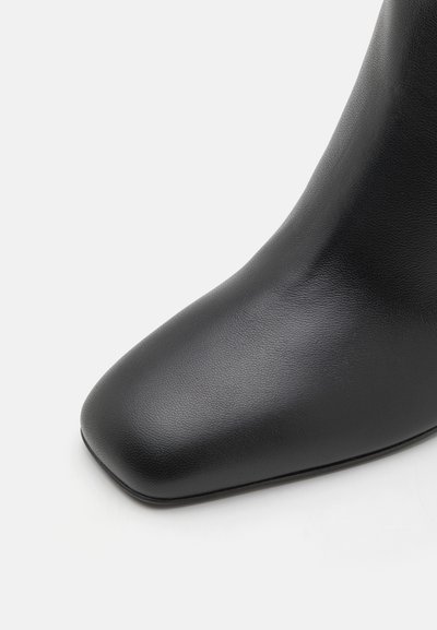 Black leather ankle boot with a sleek, smooth texture, pointed toe, and a tapered design, emphasizing a modern silhouette.