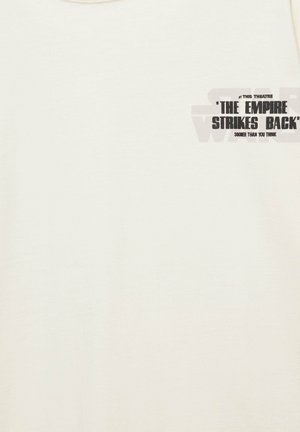 Chemise écrue avec petit texte noir en haut à gauche : « ‘The Empire Strikes Back’ bientôt dans ce théâtre, plus tôt que vous ne le pensez. »