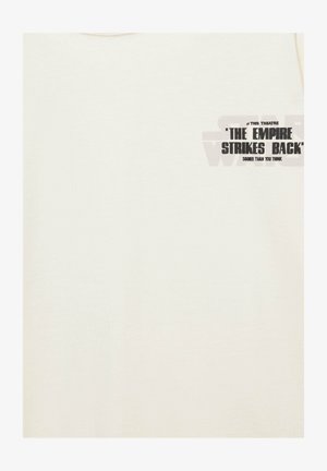 Chemise écrue avec petit texte noir en haut à gauche : « ‘The Empire Strikes Back’ bientôt dans ce théâtre, plus tôt que vous ne le pensez. »
