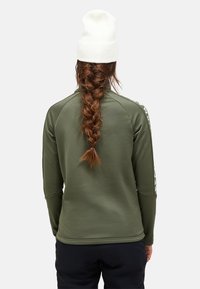 Olijfgroen sporttop met lange mouwen, een getailleerd ontwerp en logo-accenten aan de zijkant. Heeft een soepele textuur en een hoge kraag voor extra warmte.