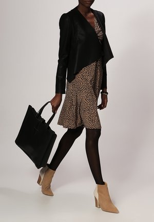 Black cropped jacket over a brown leopard print dress, paired with opaque tights and two-tone ankle boots. A black tote bag is held in one hand.