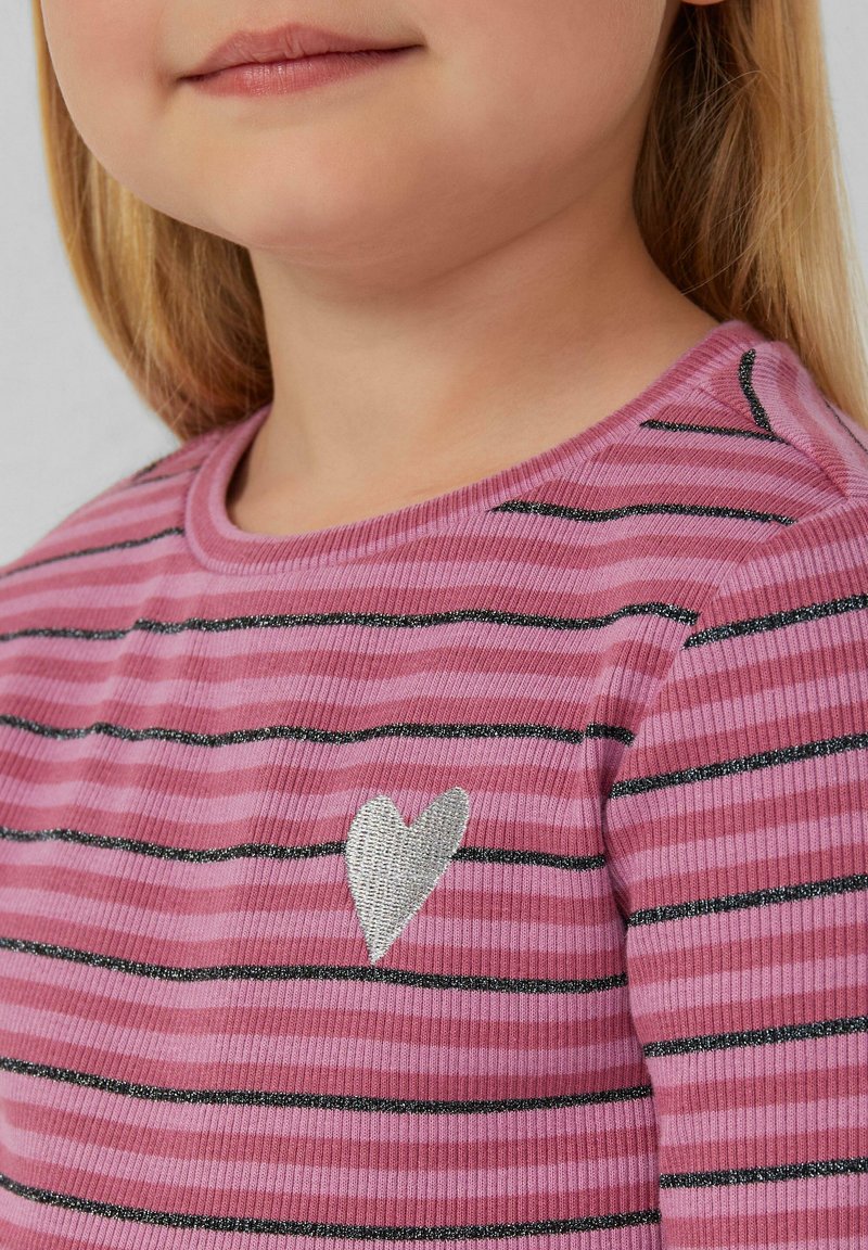 Rozā svītrainā krekla dizains ar melnām horizontālām līnijām, kuram ir sudraba sirds uzplecs. Materiāls ir riboti, ar redzamu apaļu apkakli.