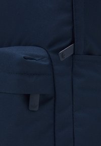 Marinblå ryggsäck med texturerad tyg, ett framfack och logotypdetaljer. Den har justerbara remmar och en hållbar design.