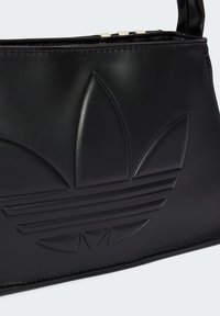 Bolsa de mão em couro preto com logótipo estampado, forma aerodinâmica e detalhes de costura. Apresenta um design estruturado e textura suave.